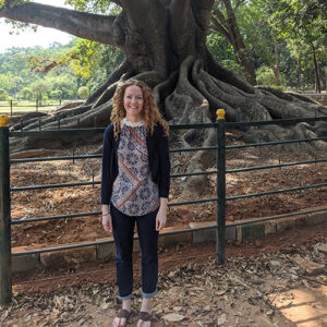 Kristin Williams, the Sustainability co-chair, is shown smiling and standing in front of a centuries old tree in India.